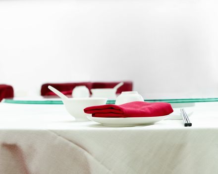 Table setting on an elegant, white dining table in a Chinese restaurant with red napkins