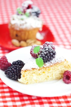 muffin with whipped cream, cake with icing, raspberry, blackberry and mint on a plate on plaid fabric