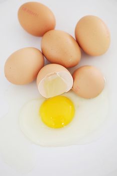 One cracked egg with its white and yolk spilling out in a group of fresh farm eggs, high angle view on a white surface