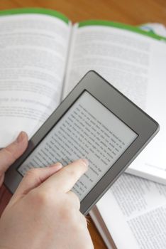 Man hands holding  an electronic book reader with text on the screen, open books in the background