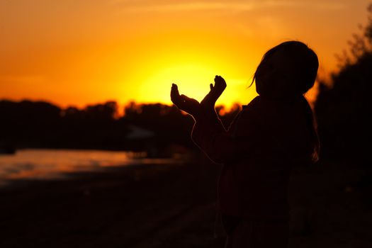 little girl holding in hands the setting sun