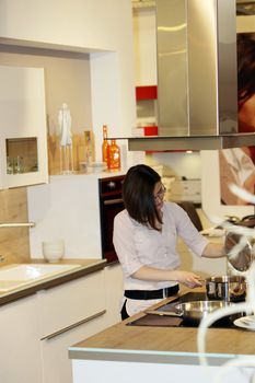 Long distance view of a stylish young housewife cooking in a modern kitchen busy moving saucepans on the stove