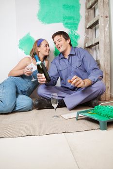 Happy couple sitting on floor and having champagne