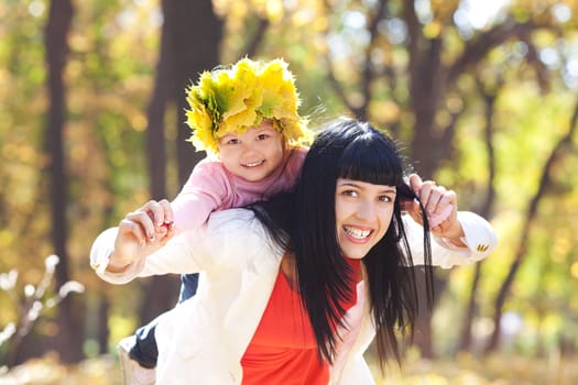 beautiful young mother holding her daughter in a wreath of maple leaves on back