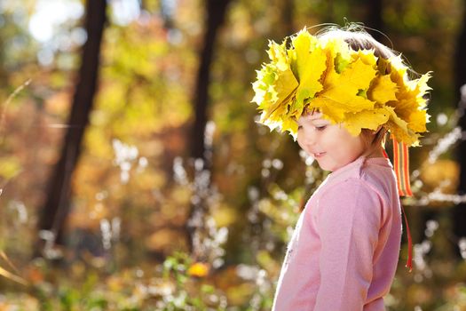 beautiful little girl in a wreath of maple leaves in autumn forest