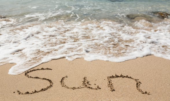 Sand drawing on warm beach by ocean surf in Caribbean spelling Sun