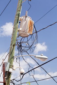 Complicated wiring forms tangled mess on power pole with light and camera