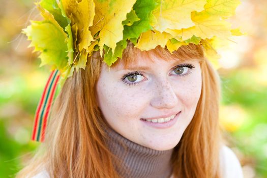 portrait of a beautiful young redhead teenager woman in a wreath of maple leaves