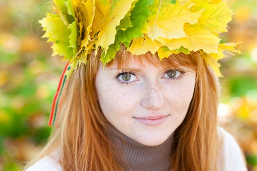 portrait of a beautiful young redhead teenager woman in a wreath of maple leaves