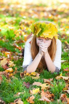 young redhead teenager woman in a wreath of maple leaves lying on the grass