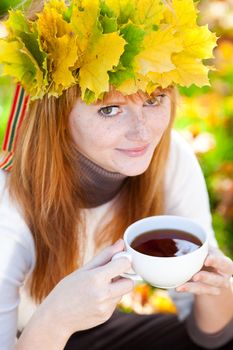 young redhead teenager woman in a wreath of maple leaves with cup of tea