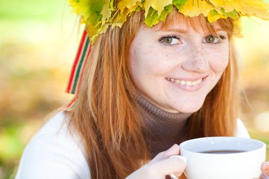 young redhead teenager woman in a wreath of maple leaves with cup of tea