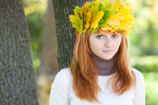 portrait of a beautiful young redhead teenager woman in a wreath of maple leaves