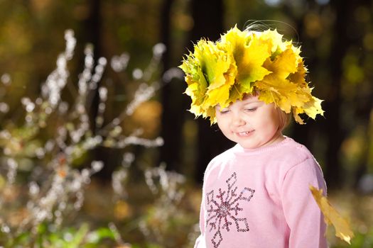 beautiful little girl in a wreath of maple leaves in autumn forest