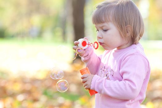 beautiful little girl making  bubble blower on the autumn forest