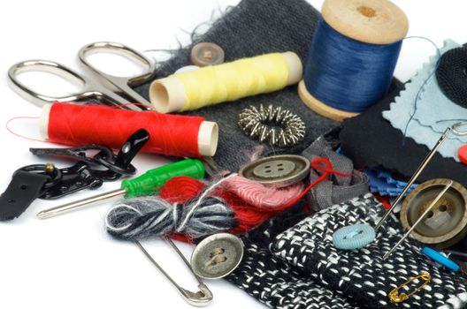 Sewing Items with Various Buttons, Pins, Spools, Threads, Scissors and Textile closeup on white background