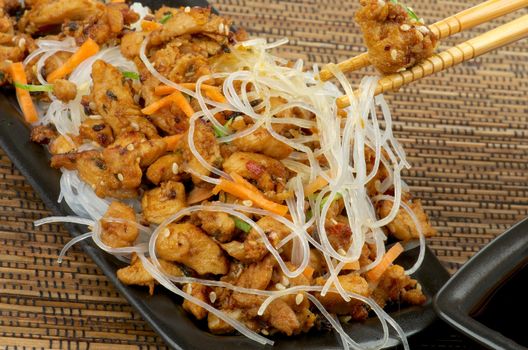 Teriyaki and Picked up Piece of Chicken From Bowl by Pair of Chopsticks closeup on Straw mat background