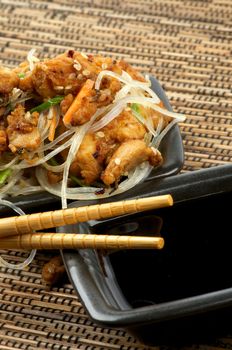 Chicken Teriyaki and Soy Sauce in Black Square Shape Bowls with Pair of Chopsticks on Straw mat background