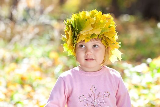 beautiful little girl in a wreath of maple leaves in autumn forest