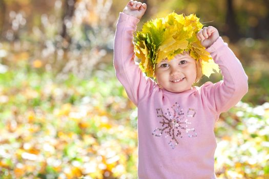 beautiful little girl in a wreath of maple leaves in autumn forest