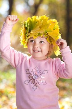 beautiful little girl in a wreath of maple leaves in autumn forest