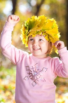 beautiful little girl in a wreath of maple leaves in autumn forest