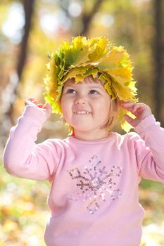 beautiful little girl in a wreath of maple leaves in autumn forest