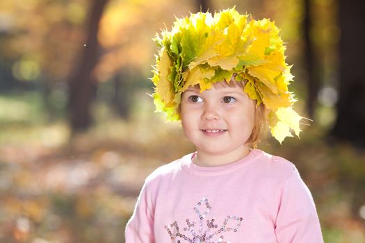 beautiful little girl in a wreath of maple leaves in autumn forest