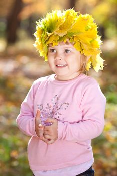 beautiful little girl in a wreath of maple leaves in autumn forest