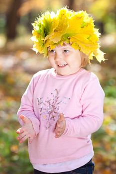 beautiful little girl in a wreath of maple leaves in autumn forest