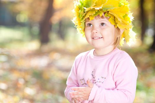 beautiful little girl in a wreath of maple leaves in autumn forest