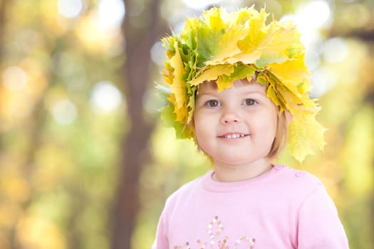 beautiful little girl in a wreath of maple leaves in autumn forest