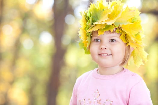 beautiful little girl in a wreath of maple leaves in autumn forest