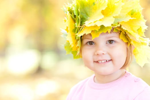 beautiful little girl in a wreath of maple leaves in autumn forest