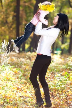 beautiful young mother holding her daughter in a wreath of maple leaves 