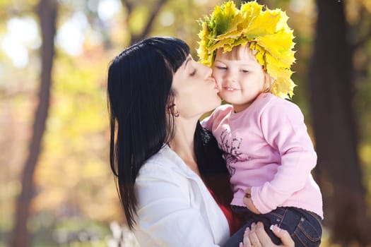 beautiful young mother holding her daughter in a wreath of maple leaves 