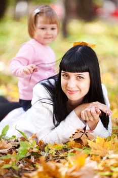beautiful young mother and her daughter lying on the autumn leaves