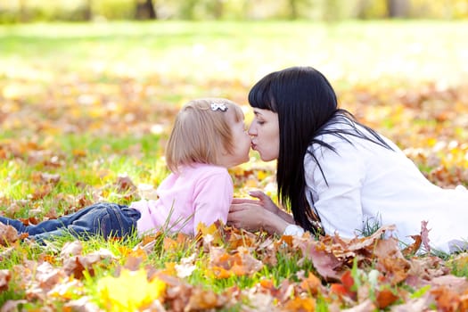 beautiful young mother and her daughter lying on the autumn leaves