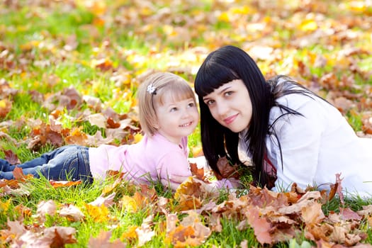 beautiful young mother and her daughter lying on the autumn leaves