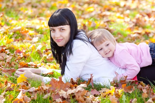 beautiful young mother and her daughter lying on the autumn leaves