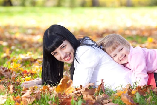 beautiful young mother and her daughter lying on the autumn leaves