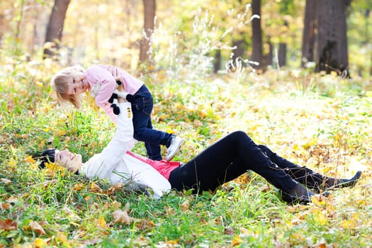 beautiful young mother and her daughter lying on the autumn leaves