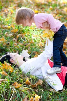 beautiful young mother and her daughter lying on the autumn leaves