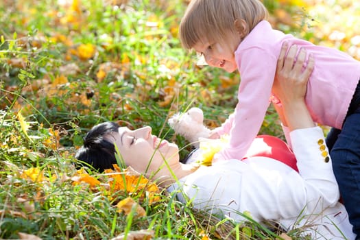 beautiful young mother and her daughter lying on the autumn leaves