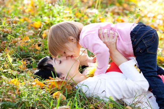 beautiful young mother and her daughter lying on the autumn leaves