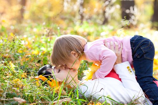 beautiful young mother and her daughter lying on the autumn leaves