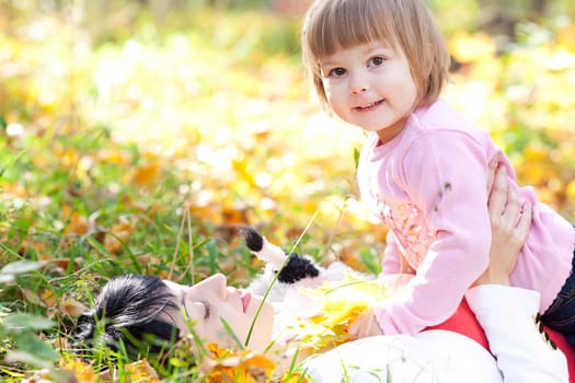 beautiful young mother and her daughter lying on the autumn leaves