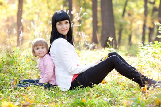 beautiful young mother and her daughter sitting on the autumn leaves