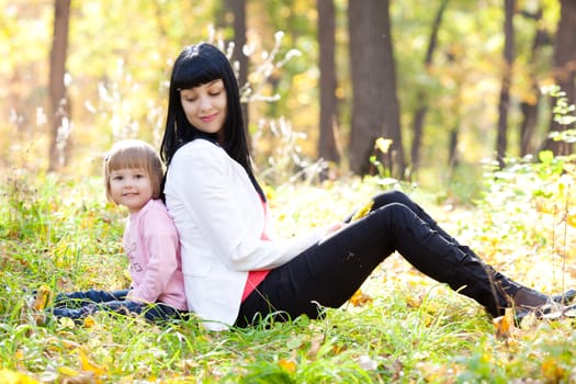 beautiful young mother and her daughter sitting on the autumn leaves