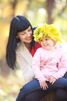 beautiful young mother holding her daughter in a wreath of maple leaves 